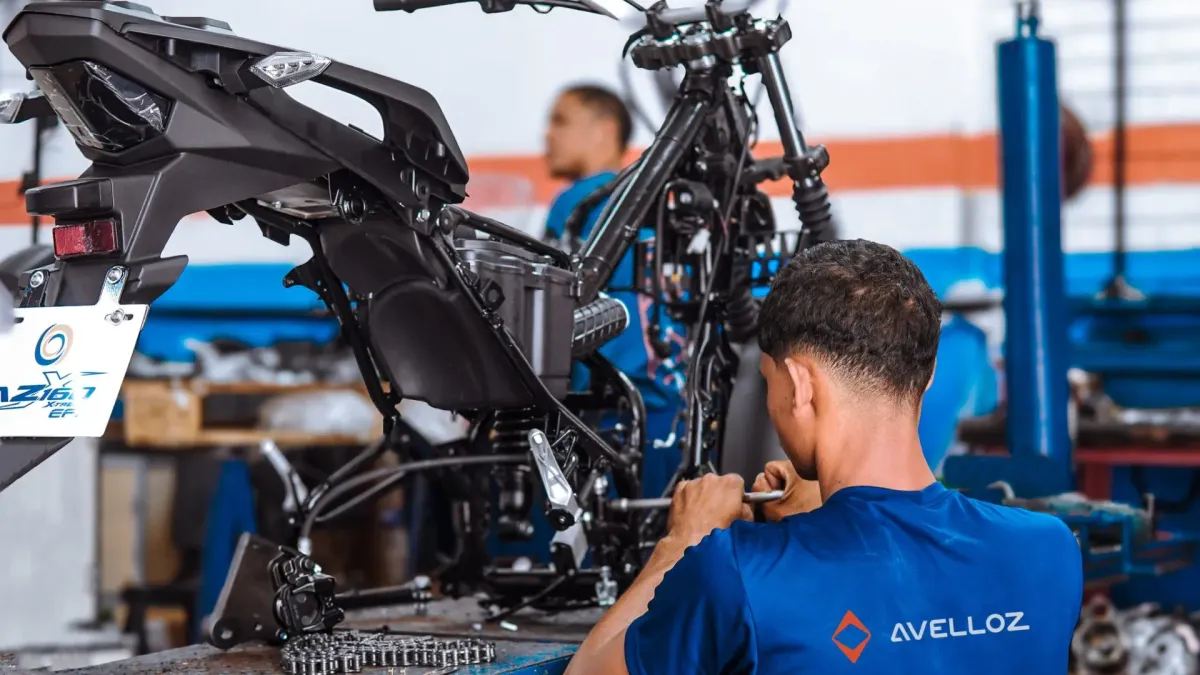 Colaborador com camisa da Avelloz trabalha na montagem de uma motocicleta em linha de produção.