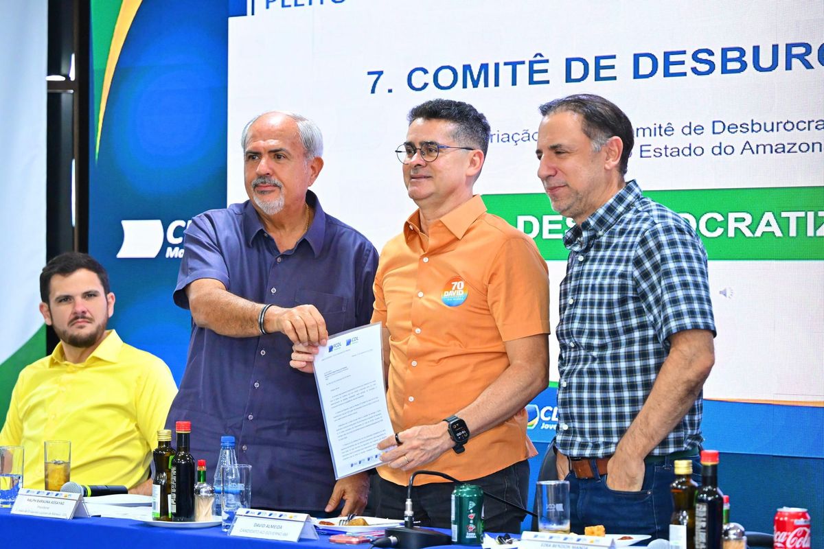 David Almeida segura documento ao lado de representantes da FCDL-AM e CDL Manaus durante evento do setor lojista.