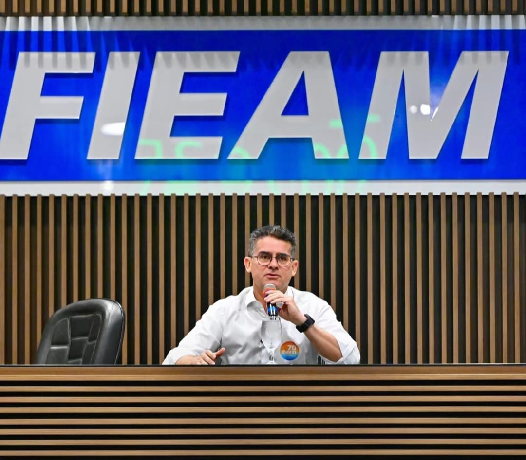 David Almeida fala ao microfone sentado à mesa sob o letreiro da Fieam, em Manaus.