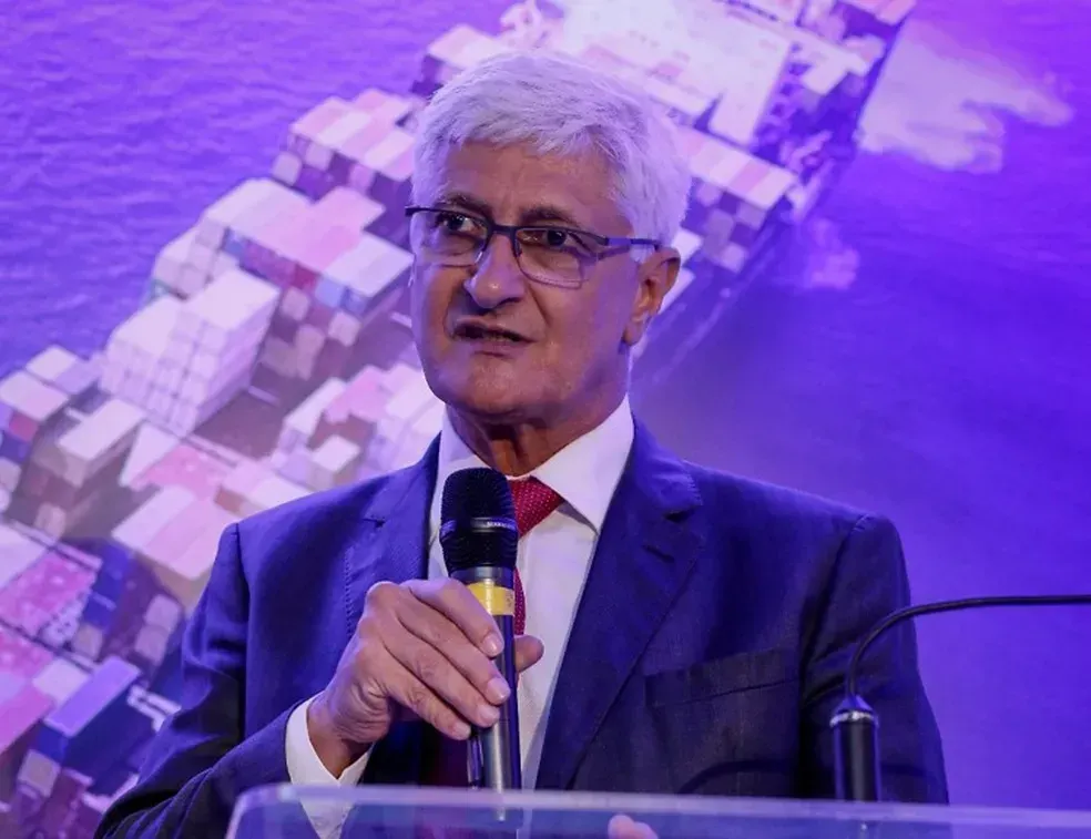 Luis Fernando Resano, diretor-executivo da Abac, fala ao microfone em evento com imagem de navio ao fundo.