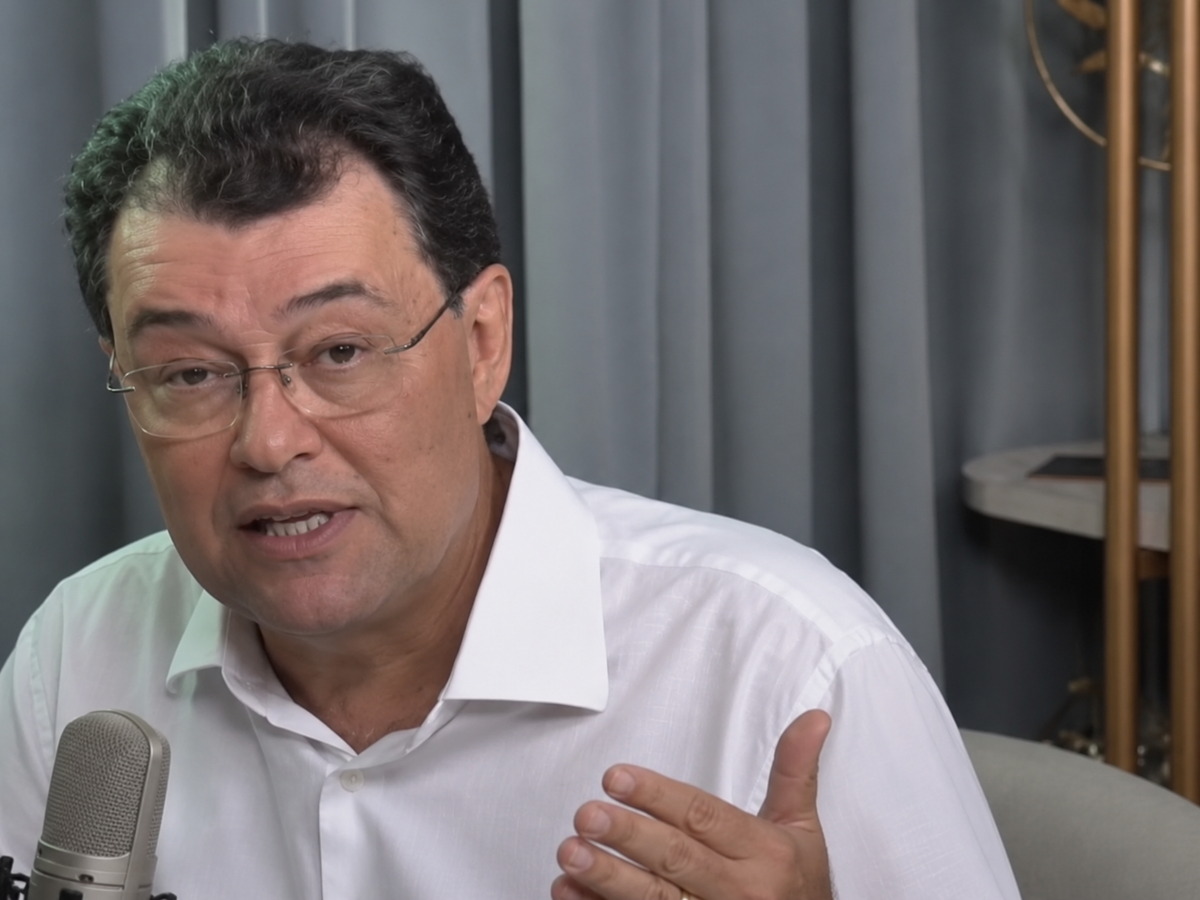 O senador Eduardo Braga, de camisa branca e óculos, fala ao microfone durante entrevista ao podcast Na Mira de Avynha.