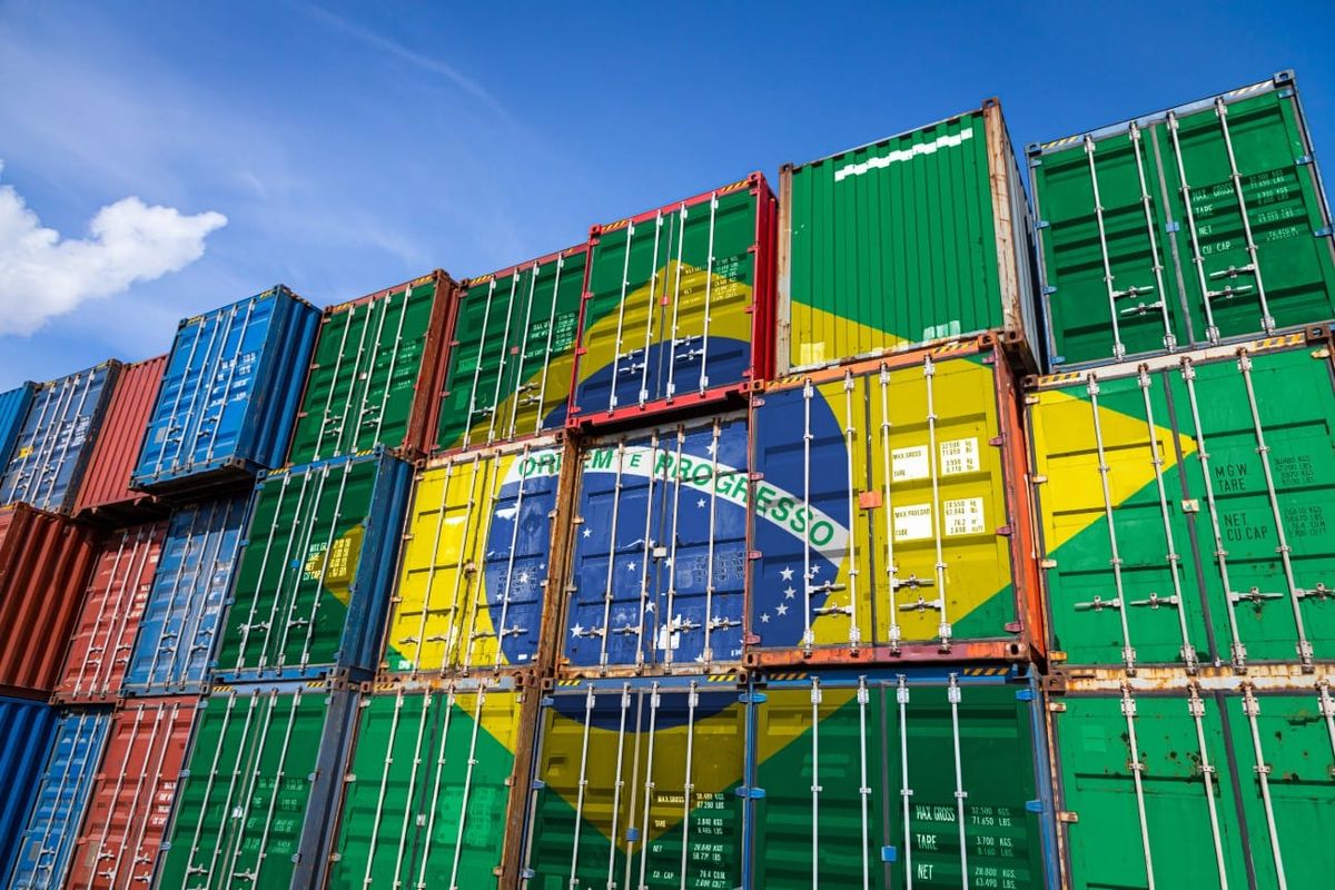 Contêineres empilhados com a pintura da bandeira do Brasil sob céu azul.