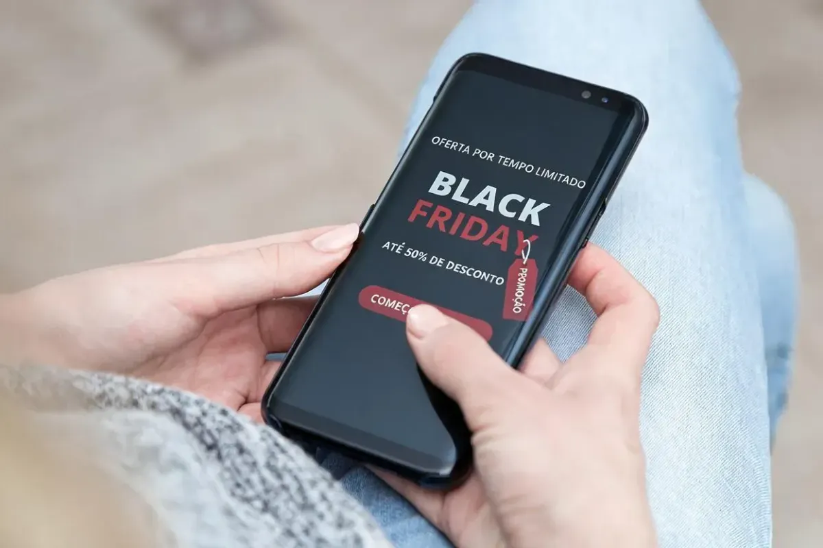Pessoa segura smartphone com anúncio de Black Friday exibindo oferta de até 50% de desconto por tempo limitado.