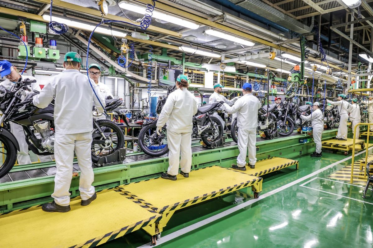 Colaboradores com uniformes brancos trabalham na linha de montagem de motocicletas na fábrica da Honda em Manaus.