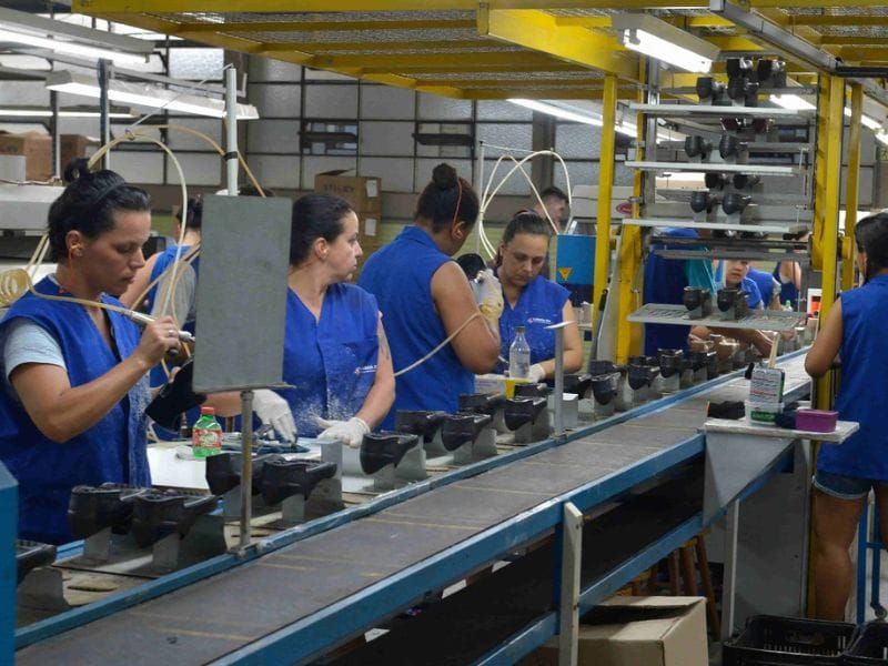 Trabalhadoras em linha de montagem industrial operando equipamentos em esteira de produção.