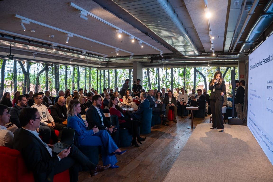 Mulher apresenta palestra para plateia sentada durante o evento Amazonas Invest Farma em São Paulo.