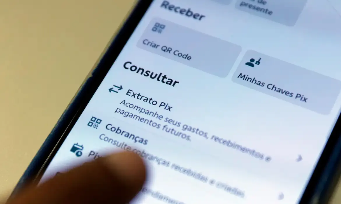Dedo de uma pessoa toca a tela de um smartphone que exibe o menu de transações do Pix em um aplicativo bancário.