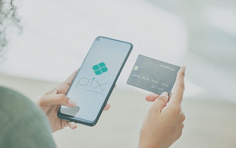 Mãos seguram um smartphone com o logotipo do Pix na tela e um cartão de crédito físico.