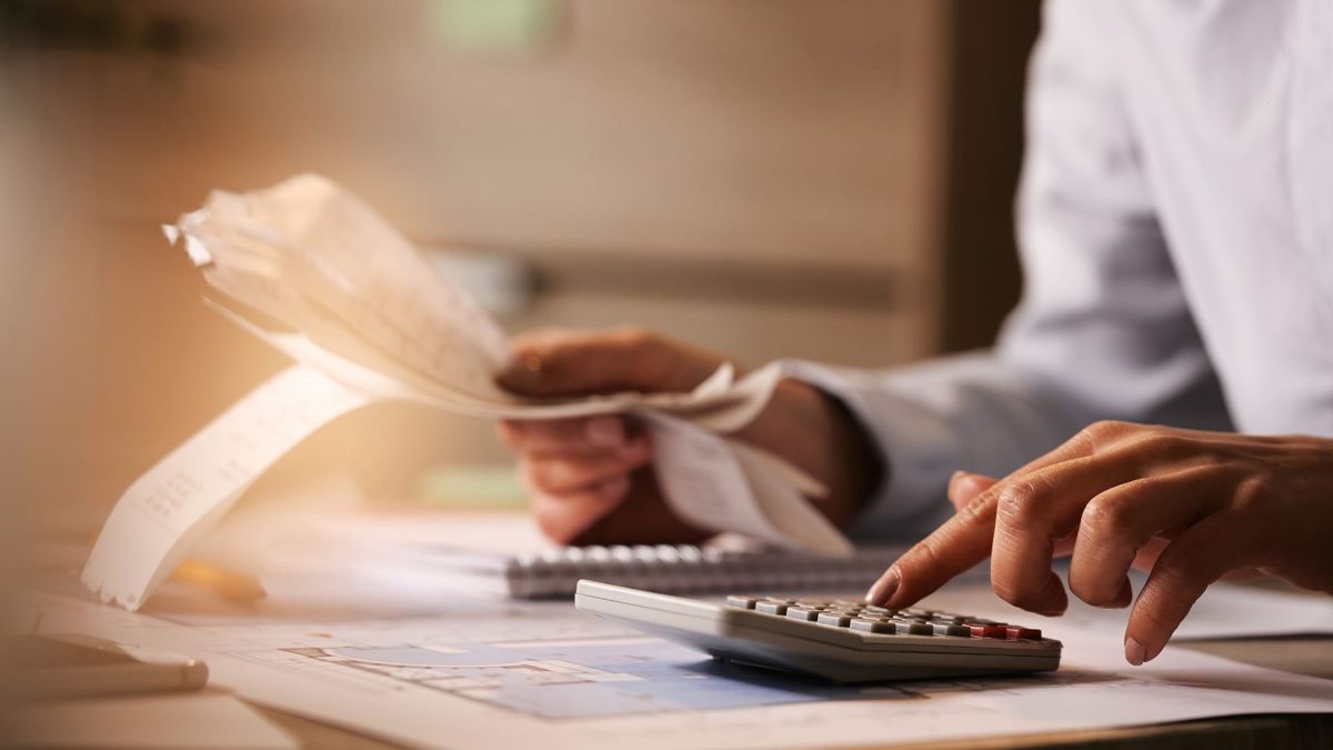 Pessoa utiliza calculadora e analisa documentos fiscais impressos sobre uma mesa de escritório.
