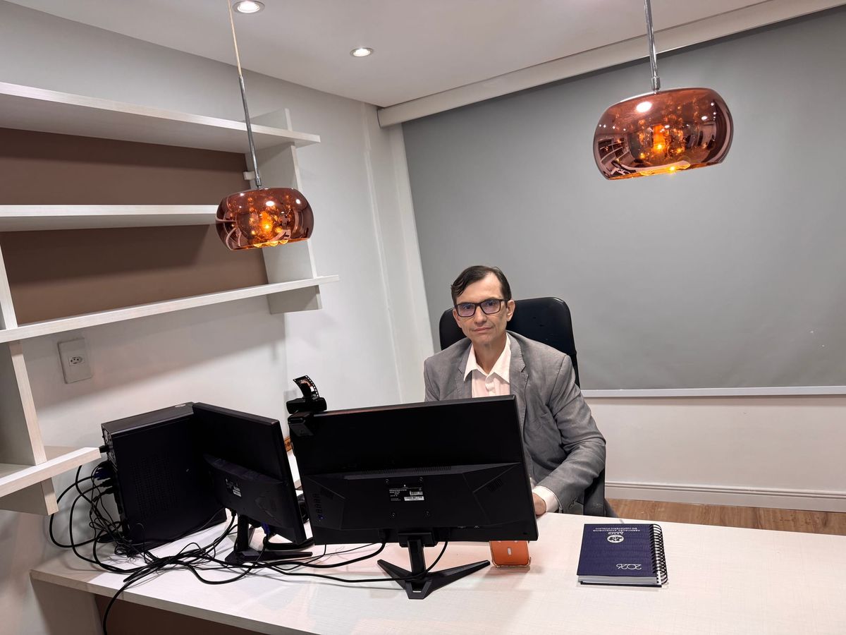 Roberto Nogueira, especialista em direito bancário, sentado em seu escritório em frente a dois monitores de computador.