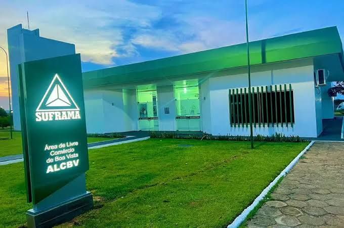 Fachada da Suframa na Área de Livre Comércio de Boa Vista (ALCBV), com gramado verde e céu ao entardecer.