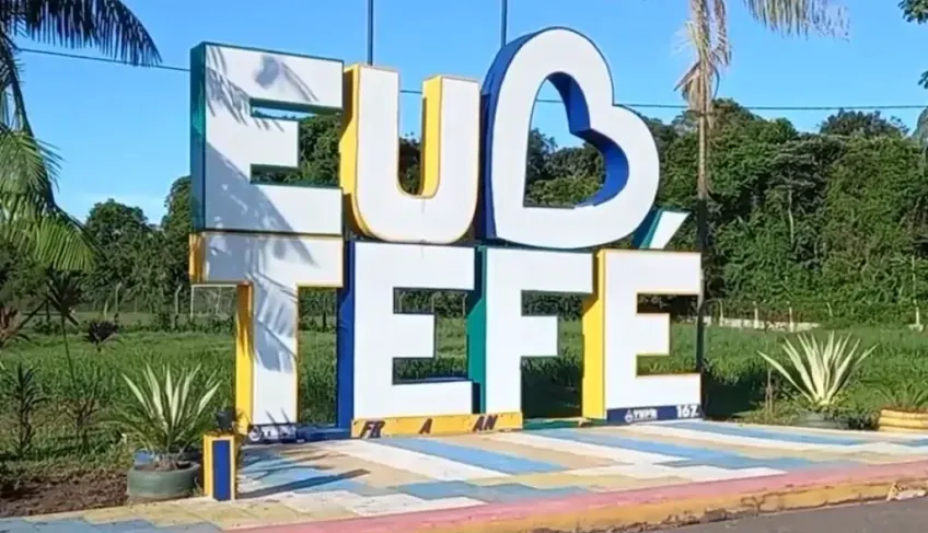 Letreiro turístico com os dizeres Eu Amo Tefé em cores azul, amarelo e branco, instalado em área aberta com vegetação.