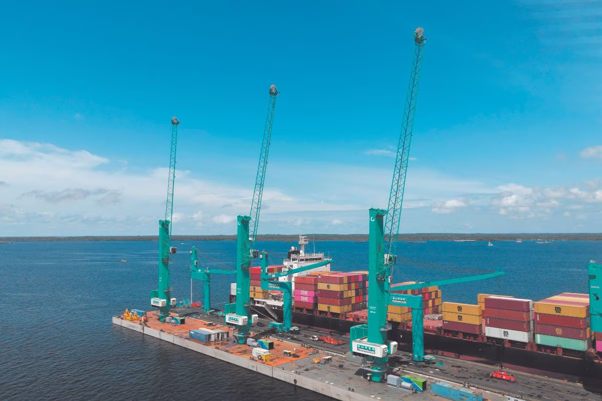 Guindastes verdes operando em píer flutuante do Super Terminais durante movimentação de navio de contêineres em Manaus.