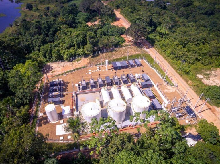 Vista aérea de usina termelétrica com tanques brancos e geradores cercada por vegetação amazônica em Codajás.