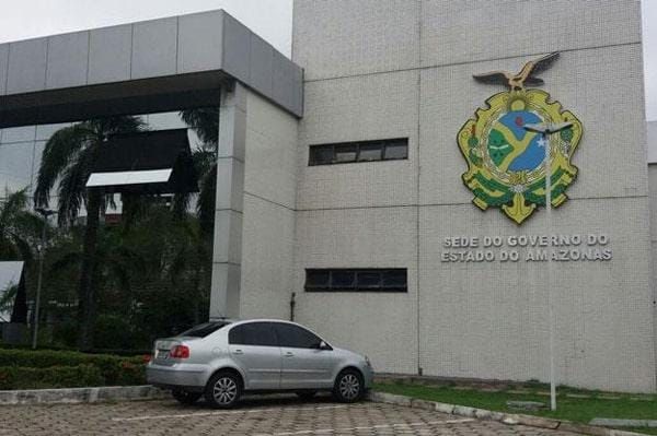 Fachada da Sede do Governo do Estado do Amazonas com brasão oficial e um carro prata estacionado à frente.