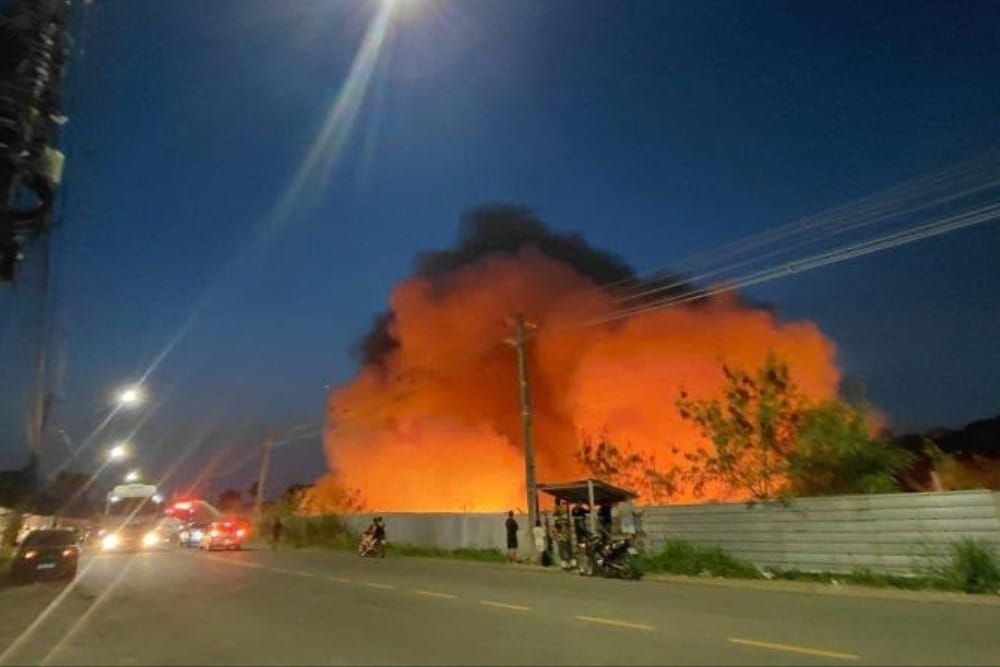 Chamas e fumaça alaranjada saindo de terreno atrás de muro no Distrito Industrial II, em Manaus, durante a noite.