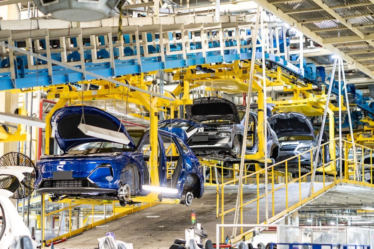 Carros em linha de montagem suspensa por estruturas amarelas em fábrica da Renault Geely do Brasil.