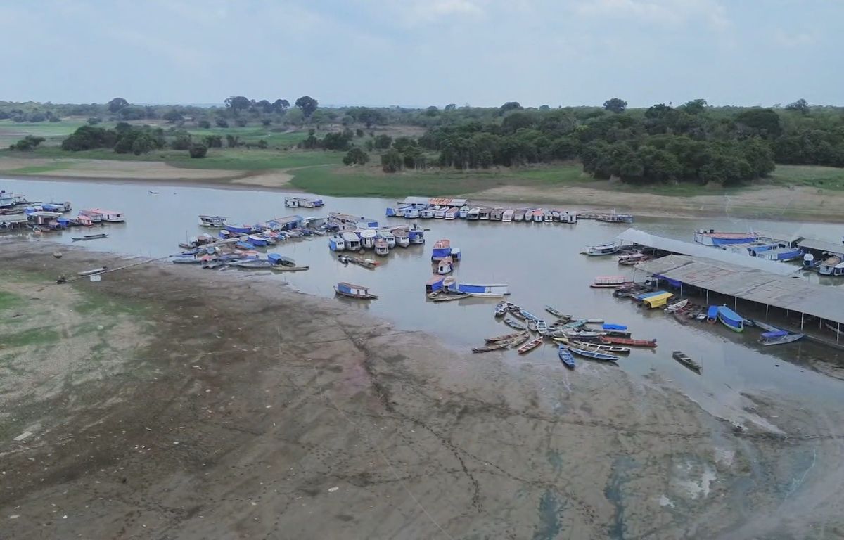 Embarcações atracadas em margem de rio com grande faixa de terra exposta devido à seca no Amazonas.