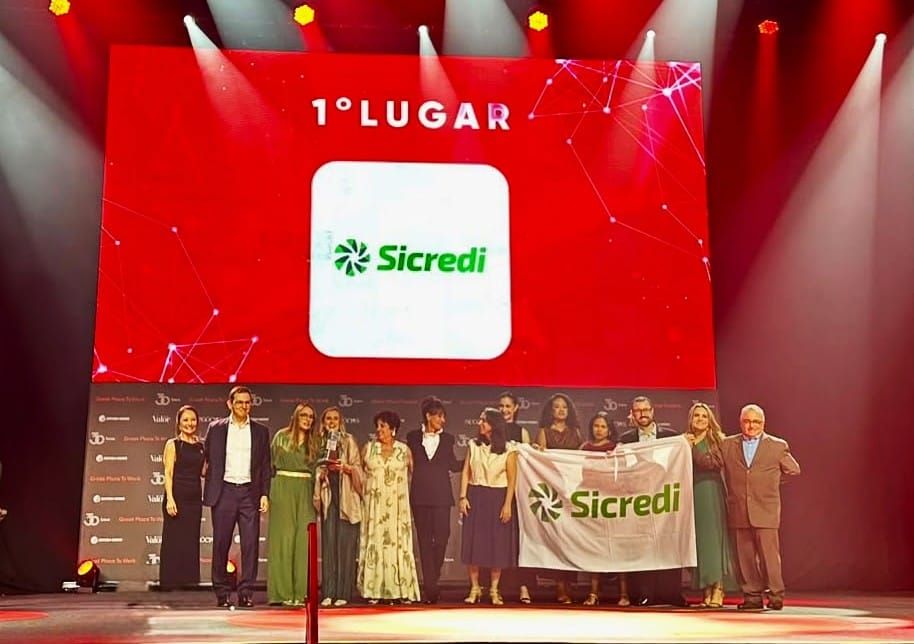 Representantes do Sicredi no palco da premiação GPTW 2026 segurando bandeira da marca diante de telão com o texto 1° Lugar.