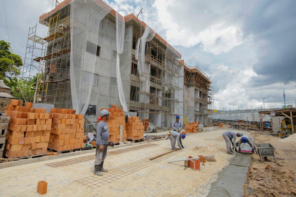 Operários trabalham em canteiro de obras de edifício residencial com andaimes e pilhas de tijolos em Manaus.