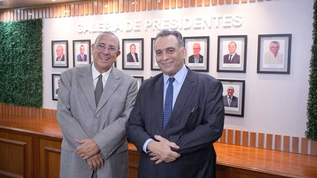 Luiz Augusto Rocha e Lúcio Flávio Morais sorrindo em frente a uma galeria de fotos de presidentes na sede do Cieam.