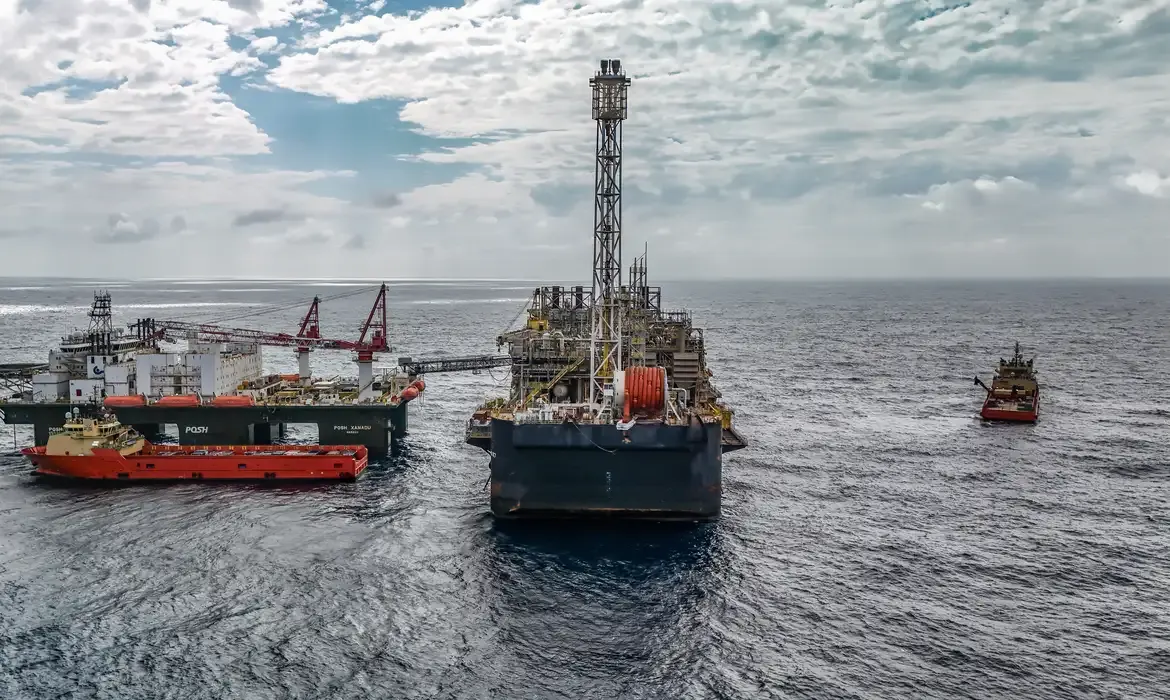 Plataforma de petróleo e embarcações de apoio em alto-mar sob céu nublado.