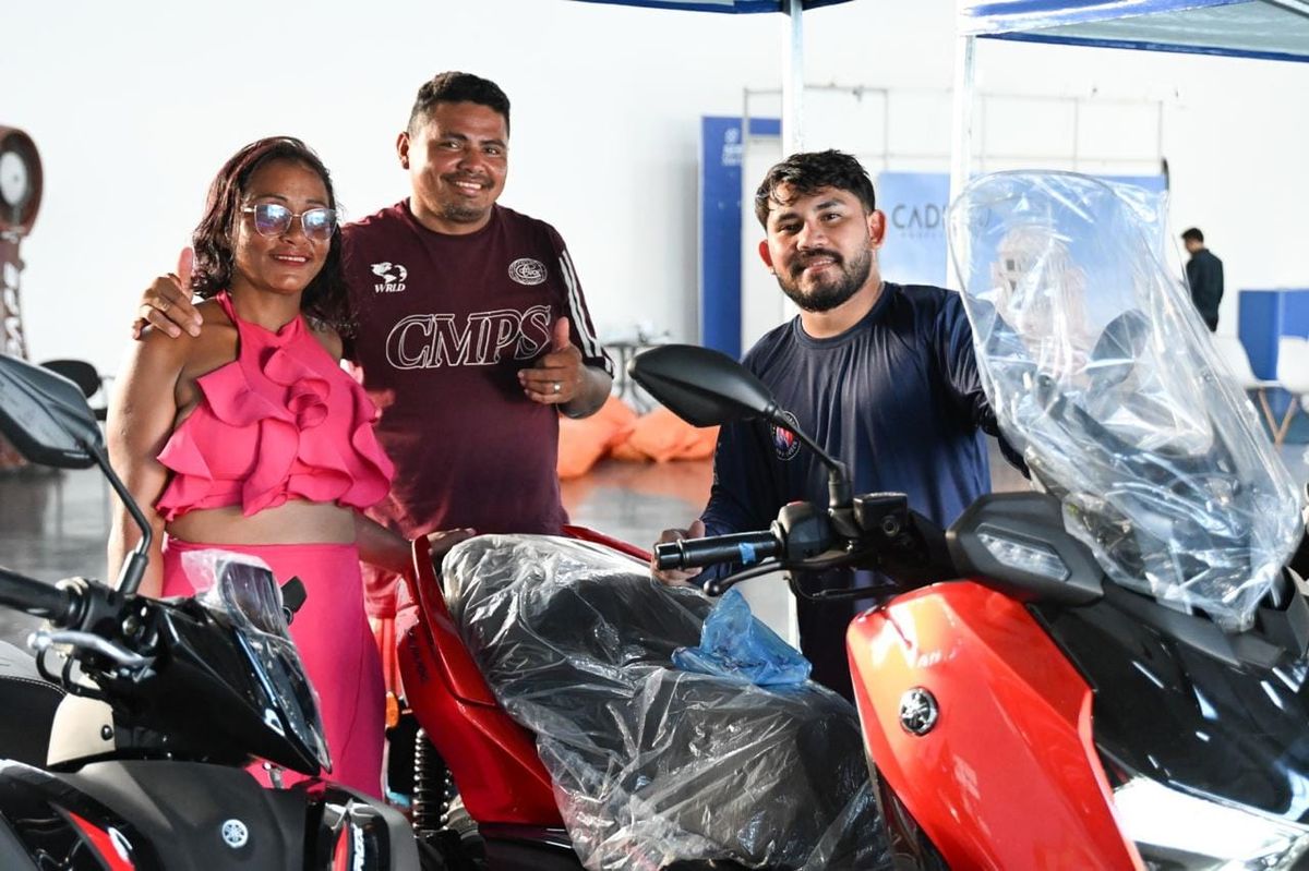 Três pessoas sorriem ao lado de motocicletas em exposição durante evento do Sebrae em Manaus.
