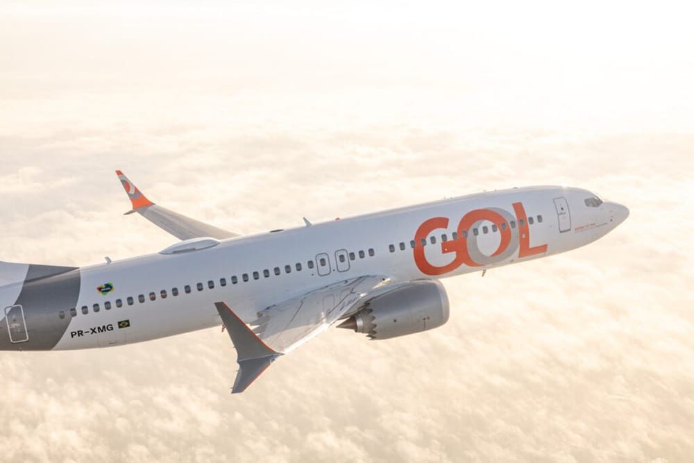 Aeronave da Gol Linhas Aéreas branca com detalhes em laranja sobrevoando nuvens.