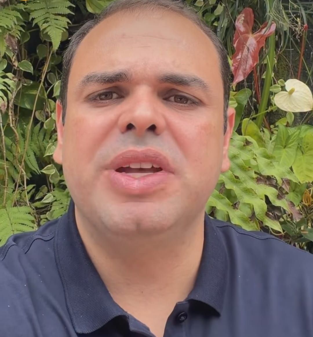 O governador do Amazonas, Roberto Cidade, fala em vídeo com fundo de folhagens verdes e flores.