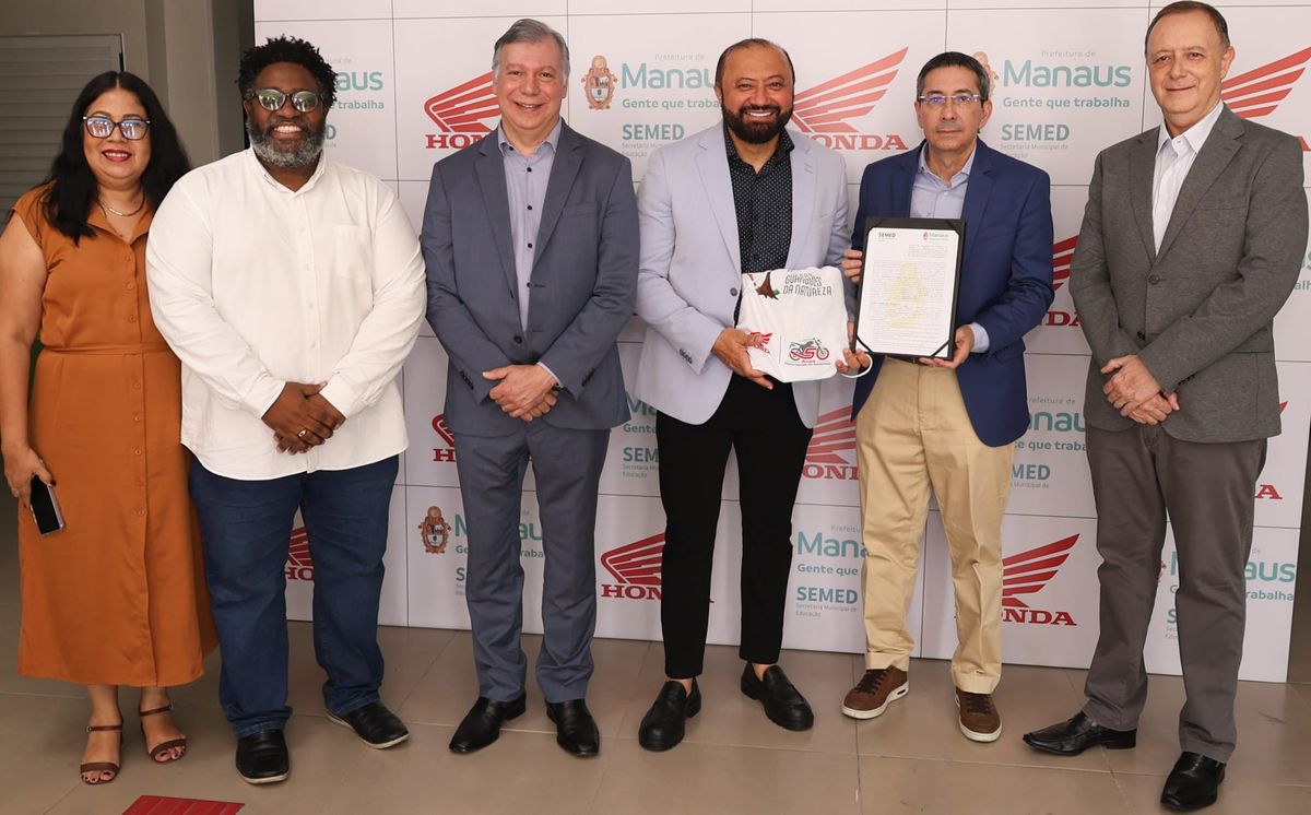 Seis representantes da Honda e da Prefeitura de Manaus posam para foto segurando o termo de cooperação e uma camiseta.