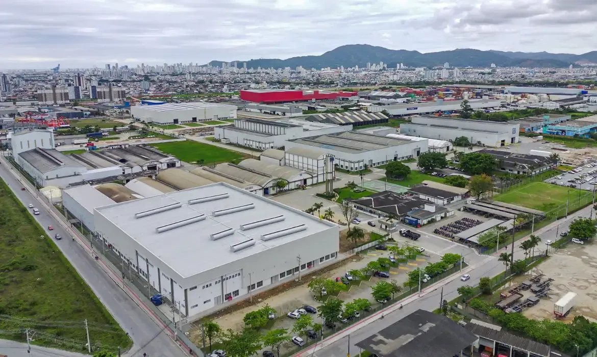 Vista aérea de galpões industriais da fábrica da WEG em Itajaí, Santa Catarina, com prédios ao fundo.