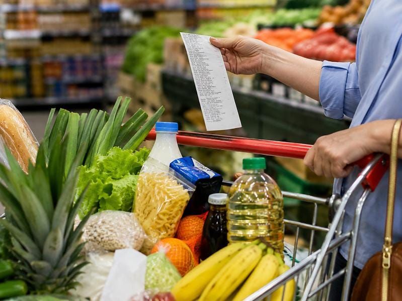 Pessoa segura nota fiscal em frente a carrinho de supermercado com frutas, legumes, óleo e macarrão em Manaus.