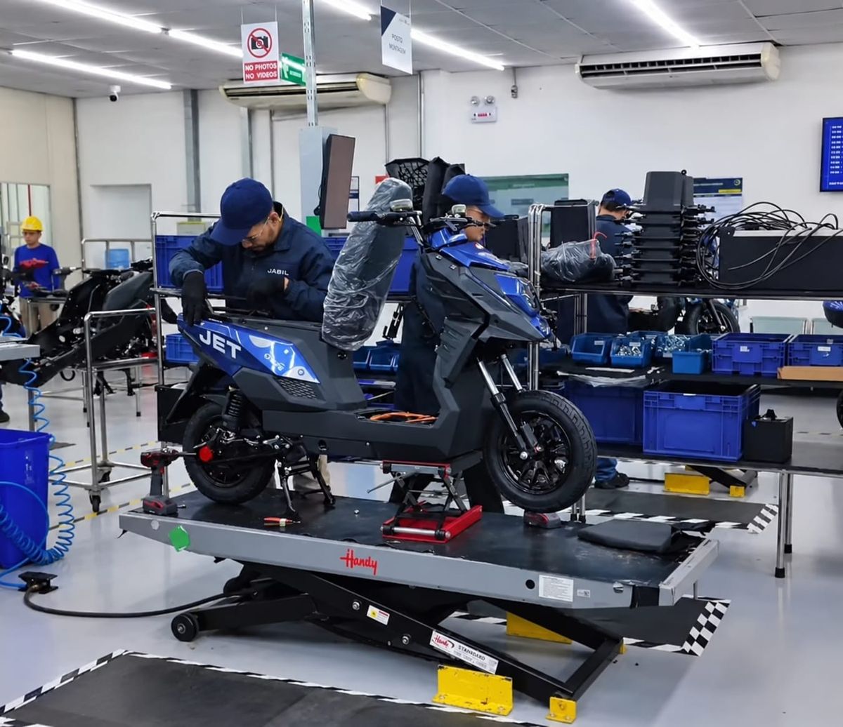Funcionários com uniformes da Jabil montando uma scooter elétrica azul modelo Jet em linha de produção em Manaus.