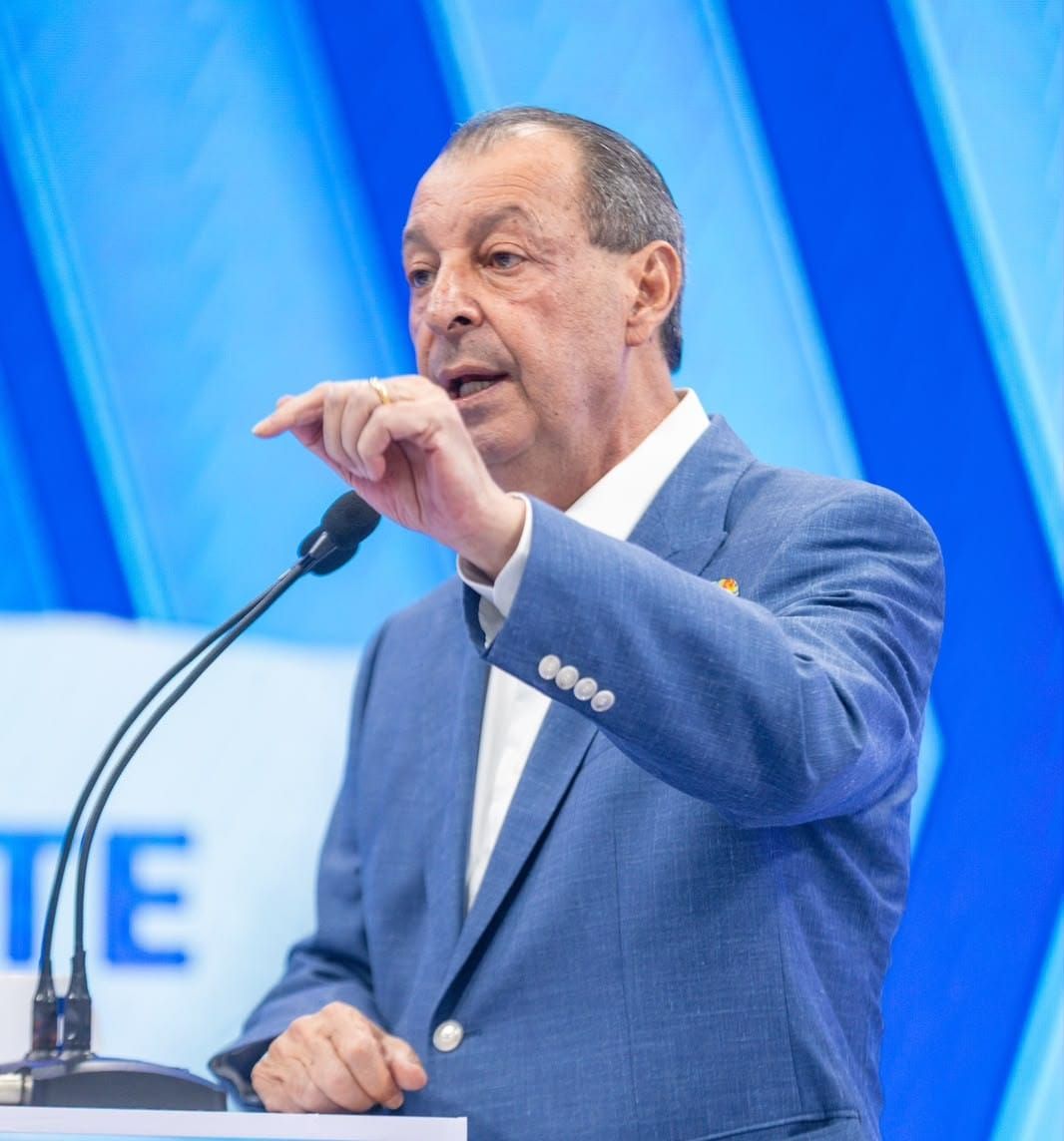 O candidato Omar Aziz, vestindo paletó azul e camisa branca, fala ao microfone durante debate em outubro de 2026.