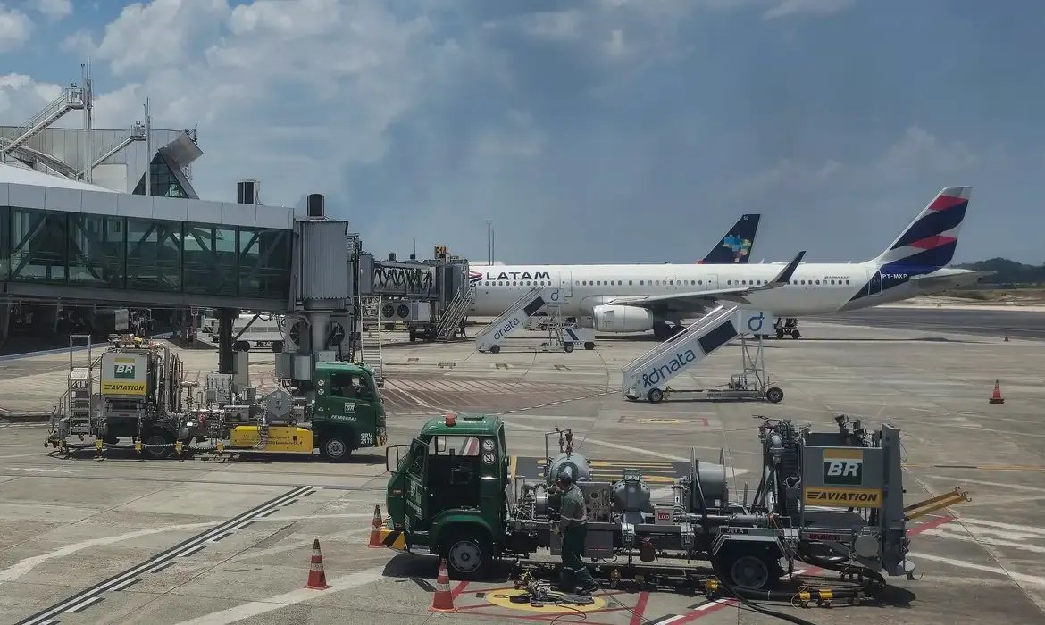 Caminhões de abastecimento da BR Aviation posicionados no pátio de um aeroporto próximo a aeronaves da Latam e Azul.