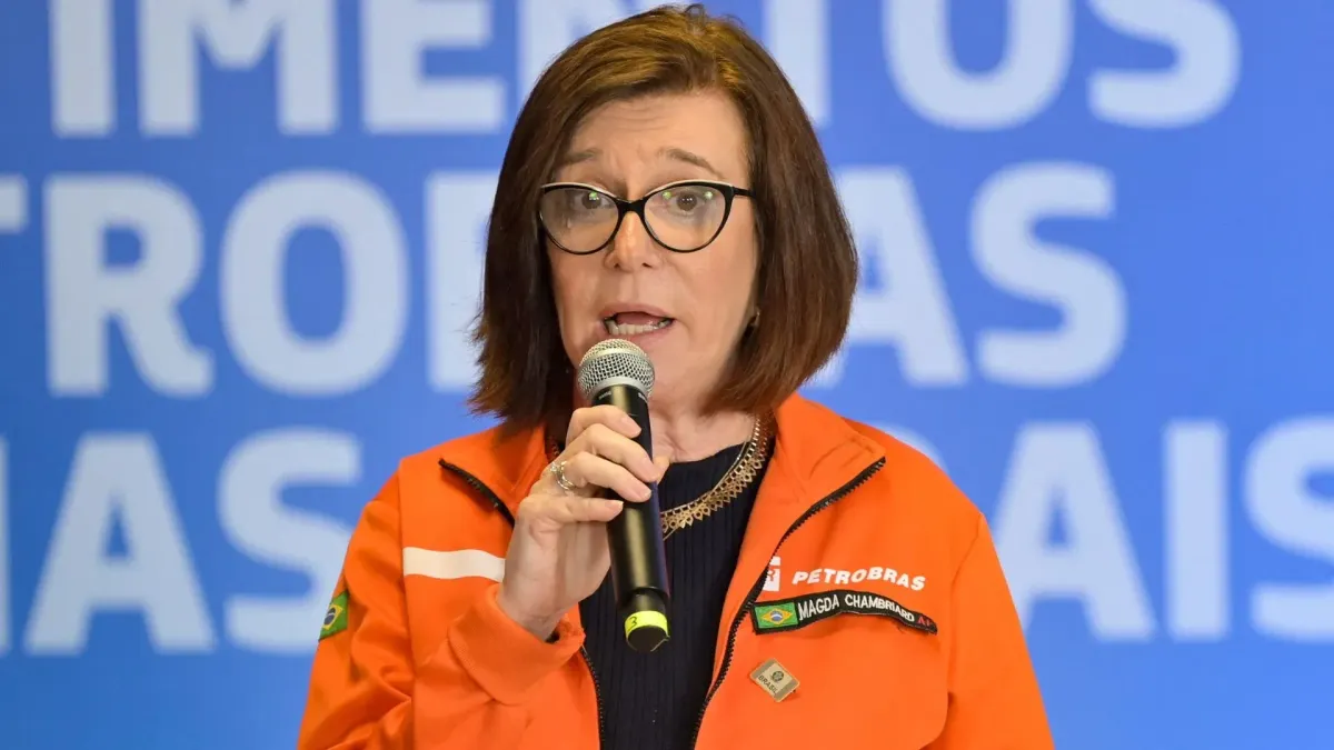 Magda Chambriard, presidente da Petrobras, fala ao microfone vestindo jaqueta laranja da companhia.