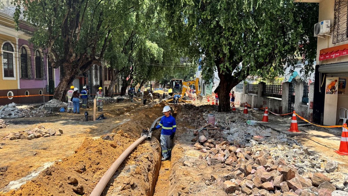 Trabalhadores em obra de escavação na rua Ferreira Pena, em Manaus, instalando nova tubulação de água sob árvores.