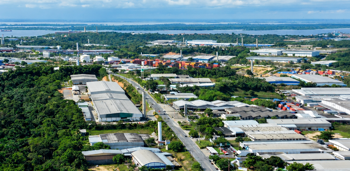Vista aérea de galpões industriais e áreas verdes no Polo Industrial de Manaus, com o Rio Negro ao fundo.