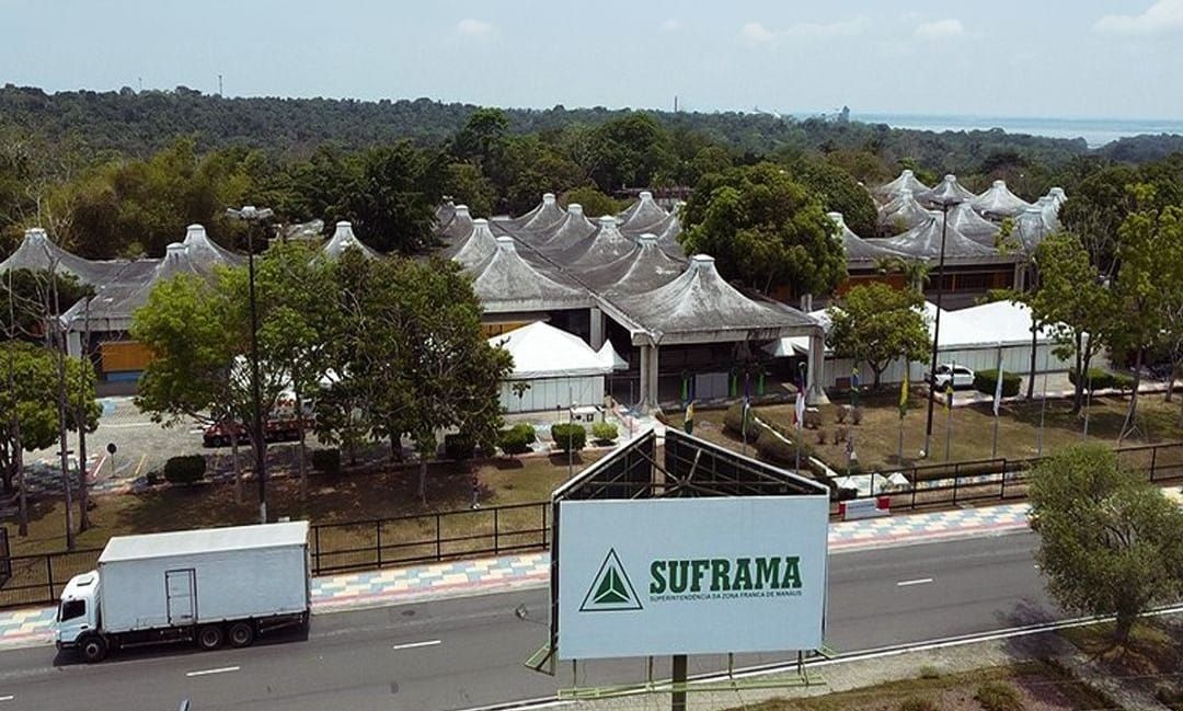 Vista aérea da sede da Suframa em Manaus, com placa da autarquia em primeiro plano e caminhão baú branco na avenida.