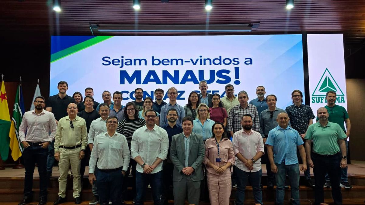 Grupo de aproximadamente 30 pessoas posa para foto em frente a um telão com a frase Sejam bem-vindos a Manaus e logo da Suframa