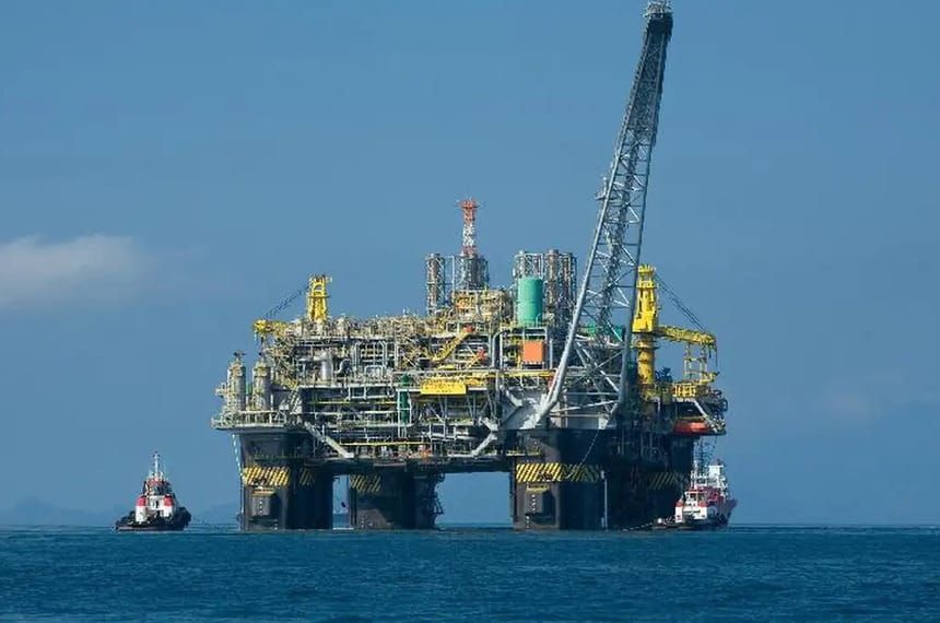 Plataforma de petróleo da Petrobras operando em alto-mar com apoio de duas embarcações rebocadoras sob céu claro.