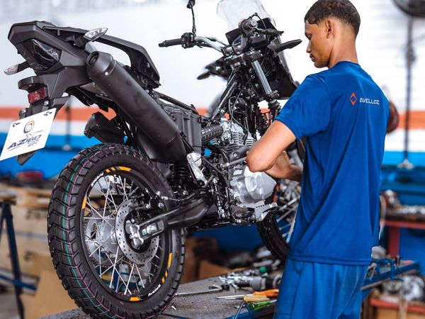Motocicleta Avelloz AZ1 branca e preta estacionada em frente a um galpão industrial, com outra moto em segundo plano