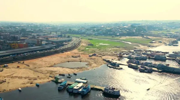 Orla de Manaus com embarcações e prédios ao fundo, sob um céu azul