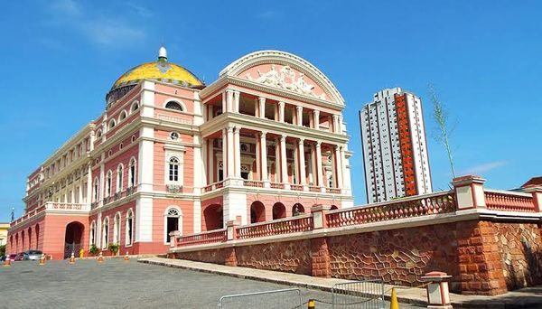 Vista frontal do Teatro Amazonas, com sua cúpula colorida e fachada em tons de rosa e branco, no Largo de São Sebastião, em