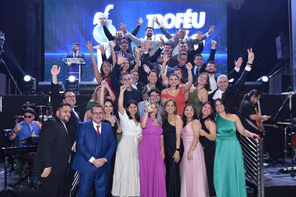 Pessoas em um evento, com um painel ao fundo exibindo o logo do Prêmio Qualidade Amazonas (PQA)