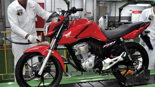 Moto Honda CG 160 Fan, na cor vermelha, estacionada em frente a uma parede de tijolos
