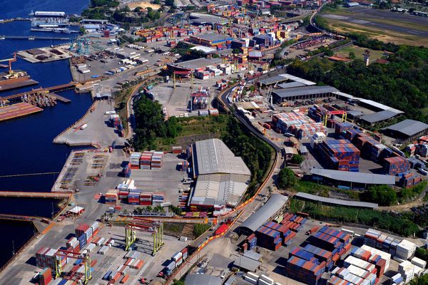 Contêineres empilhados no terminal do Super Terminais, em Manaus, com navio atracado ao fundo