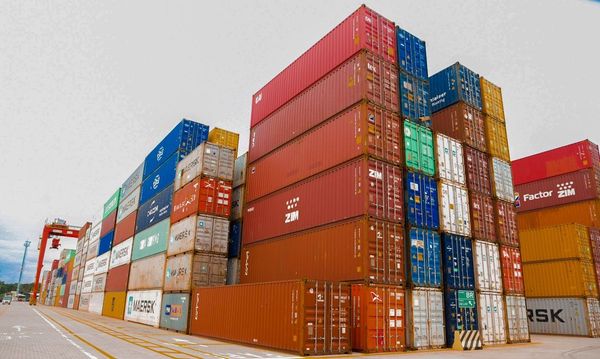 Contêineres empilhados no terminal de cargas do Polo Industrial de Manaus, com prédios de fábricas ao fundo