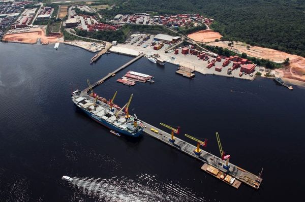 Contêineres empilhados e guindastes operando no Porto Chibatão, em Manaus, com o rio ao fundo