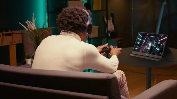 Pessoa de costas, com fones de ouvido e controle de videogame, jogando em um monitor portátil AOC 16T20E2 sobre uma mesa